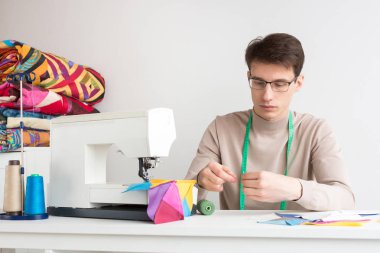 kapitone ve patchwork - yakışıklı erkek gözlük onun boynuna bir dikiş makinesi ile masa üzerinde oturan bir mezura ile iğne koydu patchwork ve makaralar iplik yakın konu.