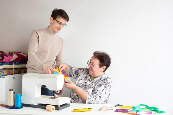 Patchwork and quilting - two smiling tailors at work in the studio with multi-colored patchwork cloth lying on the table near the sewing machine next to the thread, scissors, pins, measuring tape. — Stock Photo, Image