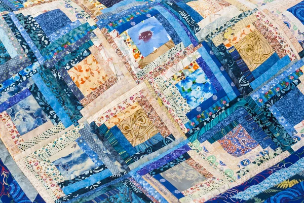 Patchwork, Handarbeit, Nähen, Interieur, Wohnkultur - bunte, volkstümliche Steppdecke in Blautönen aus kunstvollen Schnipseln mit floralen Drucken in Form von Quadraten zusammengenäht — Stockfoto