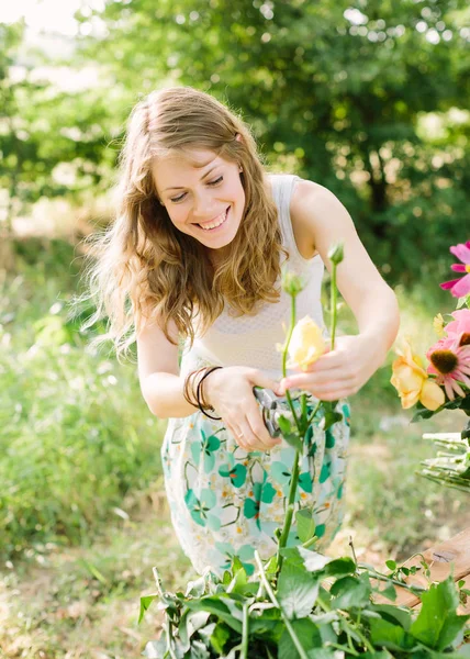 Buquê, pessoas e conceito de arranjo floral - menina bonita sorrindo jovem no jardim de verão corte folhas de rosas amarelas, uma mão segurando uma poda, olhos fechados, prepara uma flor para um buquê — Fotografia de Stock