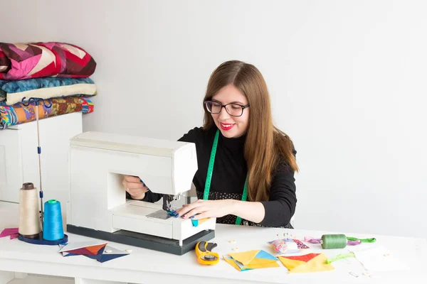 针线活和绗缝车间的一个年轻的女人-裁缝作品在一张书桌和一台缝纫机和线程、 面料、 针、 针、 按钮. — 图库照片