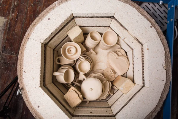 Cerámica, taller, cerámica concepto de arte - pequeño horno eléctrico para un mayor tostado de productos de arcilla sin terminar, horno para tazas y jarras sin cocer, puesta plana, vista superior . — Foto de Stock