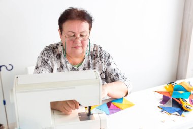 patchwork ve kapitone bir terzi kadın beyaz arka planda - atölye gözlüklü kadın patchworking için renkli kumaş dikiş makinesi artıkları üzerinde diker.