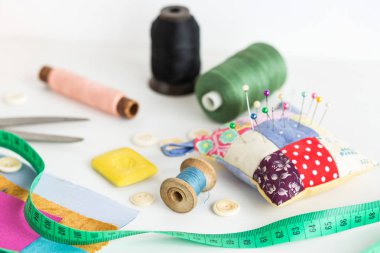 dikiş araçları, patchwork, terzilik ve moda kavramı - makas, iğne yastığı, adet renkli patchwork kumaş, sabun, ölçme metre, iş parçacığı makaralar, düğmeleri ile beyaz masa üzerinde yakın çekim.