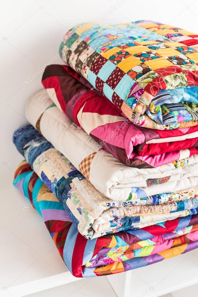 patchwork, quilting and fashion concept - close-up on beautiful colorful blankets folded and stored in several rows in height for storage, sale of stitched textile products on white background.