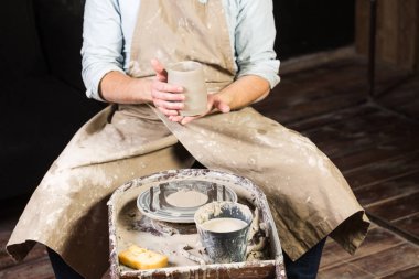 çanak çömlek, atölye, Seramik Sanat kavramı - erkek ellerini tutarak yakın çekim unfired kil Kupası, bir adam bir taze ürün işleme daha fazla önce inceliyor, ana oturur Potters tekerlek, önden görünüm.