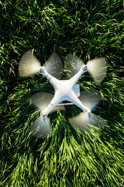 Летний полет на квадрокоптере под открытым небом, воздушные образы и концепция отдыха - превосходный современный белый высокотехнологичный беспилотник, летящий на малой высоте на фоне зеленого поля травы, вид сверху, вертикальный
.