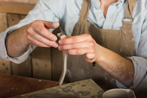 potter, stoneware, ceramics art concept - close-up on master hands working with some piece of clay, male works at a workshop near table, craftsman fingers forming the handle from raw fireclay.