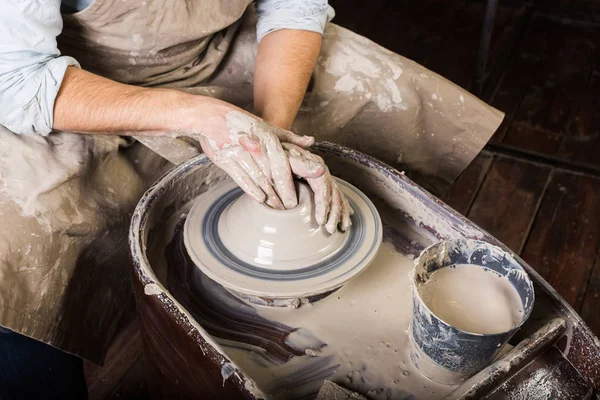 Keramiek kunst concept - close-up op werken van pottenbakkers wiel met ruwe klei en handen van de man, een man, aardewerk, workshop beeldhouwen een gebruiksvoorwerp met vingers, meester in de schort, bovenaanzicht. — Stockfoto