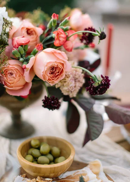 Bruiloft decor. Perfect ingericht vakantie tafel voor twee met mooie bloem samenstelling van verse bloemen in een vaas vintage, rode kaarsen, dun gesneden jamón, groene olijven en vers brood. — Stockfoto