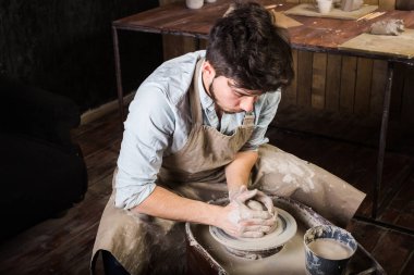 çanak çömlek, atölye, Seramik Sanat kavramı - el ile ham kil ile potters tekerlek üzerinde çalışan erkeğin erkek esmer heykeltraşlık araçlarıyla, önlük ve bir gömlek, üstten görünüm ana ahşap masa yakınındaki bir mutfak eşyaları.