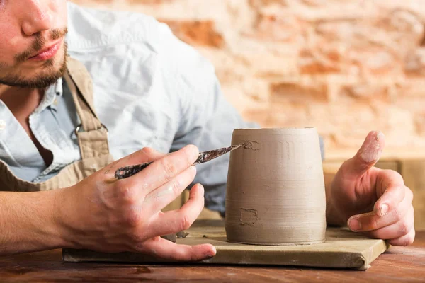 Кераміка, камінь, концепція керамічного мистецтва крупним планом на майстра нахилився над глиняною чашкою з інструментом, макрос чоловічих рук, що з'єднують шматки вогню, молодий чоловік сидить за майстернею за столом . — стокове фото