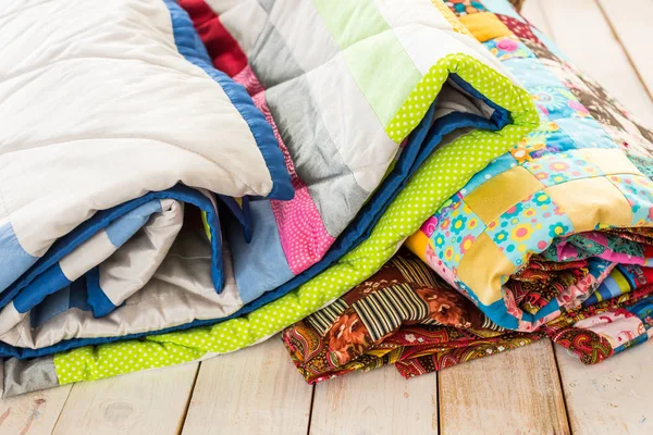 Patchwork en mode concept - close-up op mooie kleurrijke quilts gevouwen op een witte houten vloer, close-up van lappendeken producten op een witte achtergrond, bovenaanzicht, verticaal. — Stockfoto