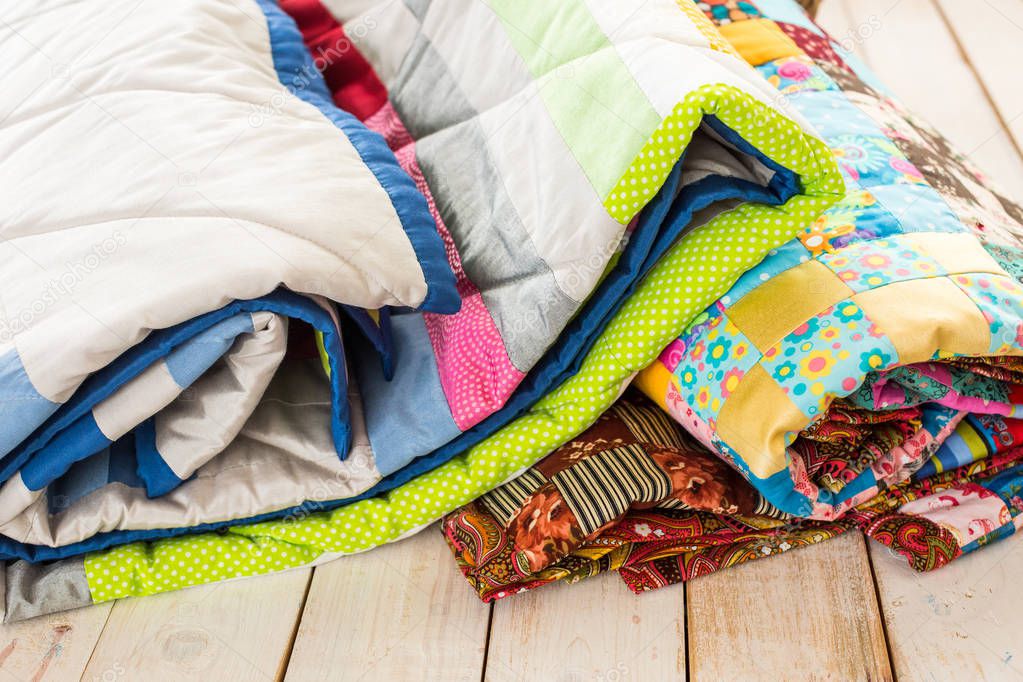 patchwork and fashion concept - close-up on beautiful colorful quilts folded on a whitewashed wooden floor, close-up on patchwork products on a white background, top view, vertical.