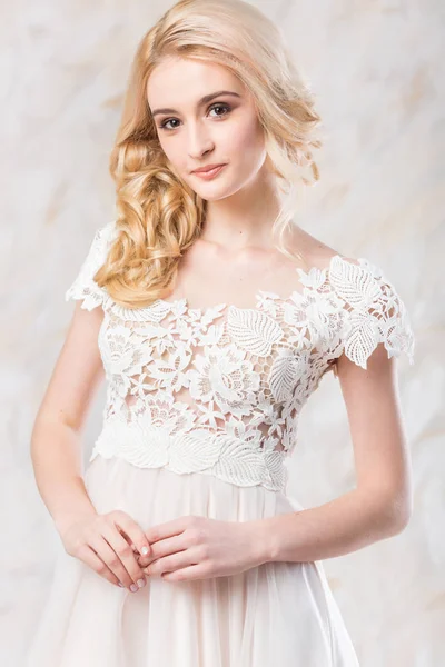 fashionable wedding dress, beautiful blonde model, bride hairstyle and makeup concept - sweetheart smiling young woman in white gown indoors on light background, lovely female posing in the studio.