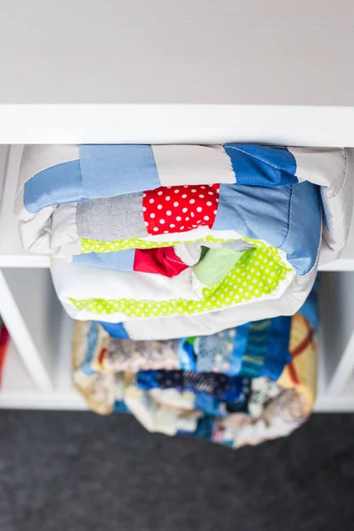 Lappendeken, naaien en mode concept - twee kleurrijke het gewatteerde spreien in de studio in witte planken afgewerkt met enkele opbergvakken, het magazijn van afgewerkte producten, bovenaanzicht. — Stockfoto