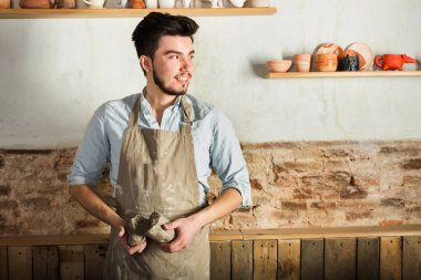 Potter, araçlar, Seramik Sanat kavramı - sakallı bir önlük giymiş esmer erkek gülümseyen genç efendi şamot, bir Fransız Atölyesi'nde hammadde ile büyük parçalarını tutan eller.