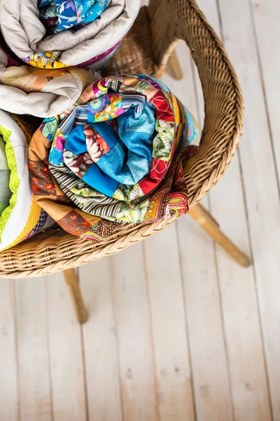 Patchwork en mode concept - close-up op drie kleurrijke quilts gerold in een buis gelegd in een rieten stoel en opslag van de eindproducten op een witte achtergrond, top uitzicht, verticale. — Stockfoto