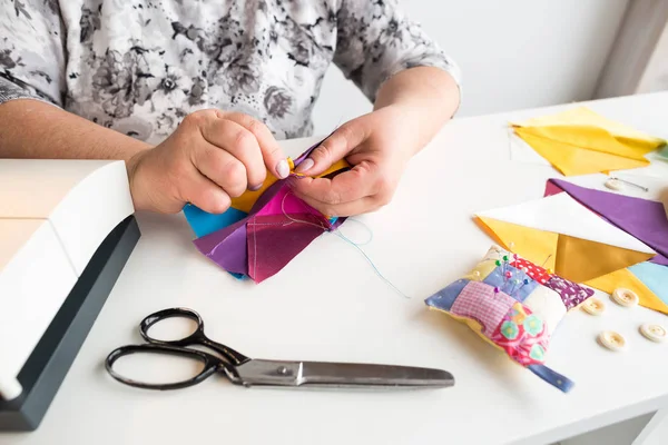 Costura y acolchado a mano en el taller de una mujer sastre - de cerca en las manos de una costurera combinar las piezas de patrón están cosidos de telas de colores en el escritorio de hilo, tijeras . — Foto de Stock