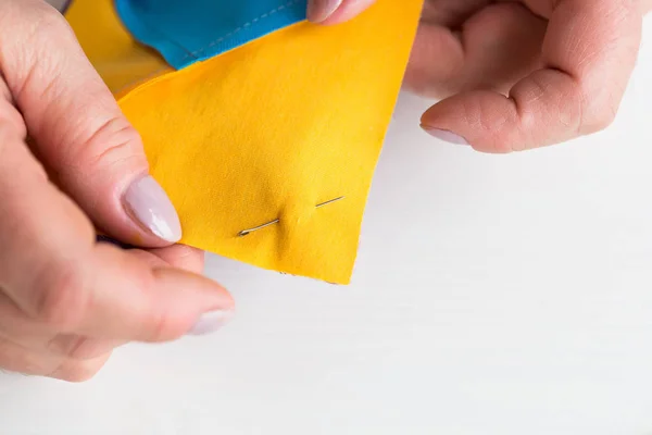 Naaien en quilten in het atelier van een kleermaker vrouw op witte achtergrond - close-up op de vingers van de kleermaker vastgemaakt met de restjes van de veiligheidsspeld van blauwe en gele stof voor patchwork. — Stockfoto
