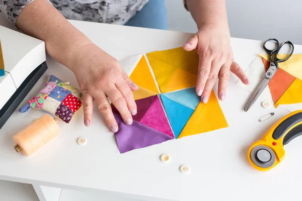 Naaien en quilten in de werkplaats van een kleermaker vrouw op witte achtergrond - op maat op het werk met stukjes gekleurde doek op de tafel met draden, stoffen, naalden, naaimachine, roterende scharen. — Stockfoto