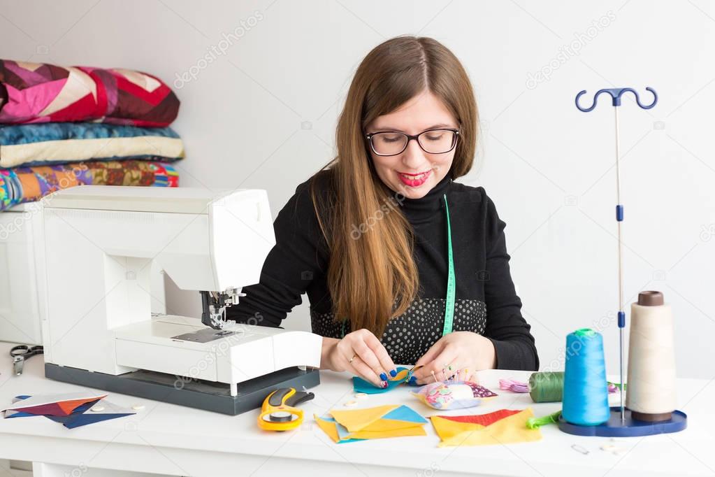 needlework and quilting in the workshop of a young woman, a tailor - young woman in glasses tailor at work with pieces of colored cloth on the table with threads, fabrics, needles and sewing machine