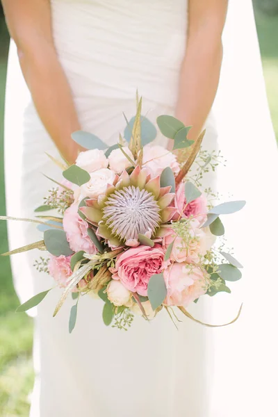 Elegante Braut in weißem Kleid und Schleier mit einem Brautstrauß aus sanft rosa Rosen, Pfingstrosen und Eukalyptus in der Hand. — Stockfoto