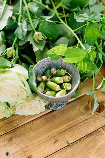 자연, 꽃 디자인, 원 예, 환경 개념-녹색 도토리와 줄기와 잎 나무 보드에 장미 크림 피 버드의 신선한 무리와 작은 금속 그릇의 근접 — 스톡 사진