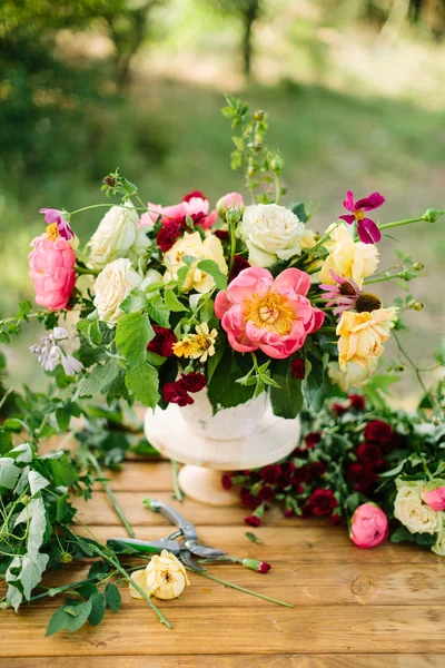 Kunsten en ambachten, bruiloft, decor, viering, zomer, natuur concept - bos van decoratieve bloemen zoals rozen, lawines, pioenrozen en diathuses, versierd met verdure, geplaatst in vaas op houten tafel — Stockfoto