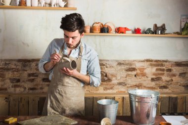 Potter, atölye, Seramik Sanat kavramı - genç ustası stand ile ham ürün, işyerindeki kil Kupası ve araçlar, iki kova su masada, holding Meksika, İspanyol craftsmans eller.