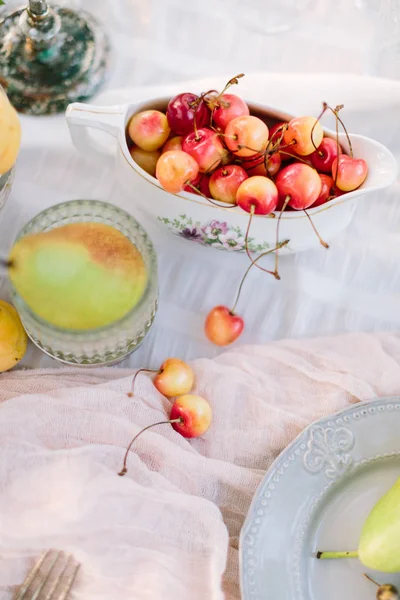 Piknik, vegetáriánus étel, holiday koncepció - érett finom piros és sárga cseresznye szárú, körte díszített asztalon fél, gyümölcsöket és ételeket, fehér terítő, tiszta és friss, lapos lay. — Stock Fotó