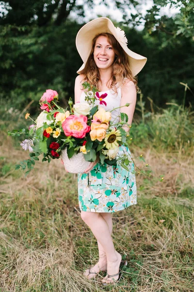 bouquet, people, flower holidays , gift and floral arrangement concept - beautiful female florist in a fashionable hat posing with bouquet of fresh flowers on background of trees, smiling woman.