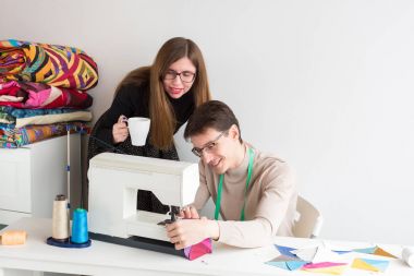 kapitone ve terzi erkek - genç güzel kadın Studio el dikiş makinesi çok renkli patchwork kumaşların üretimi için bir genç terzi adamdan işyerinde arıyorsunuz cup ile patchwork.