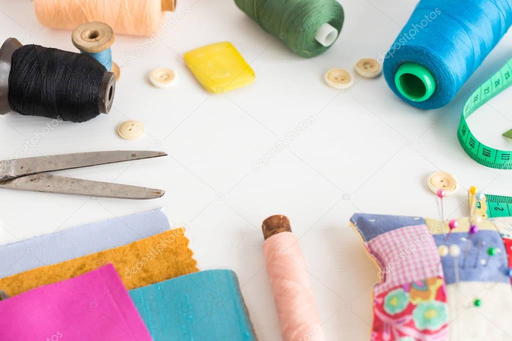 tailoring and fashion concept, patchwork, close sewing tools - working tools on a white table, thread spools, buttons, meter, pincushion, scissors, pieces of colored patchwork fabric, soap.