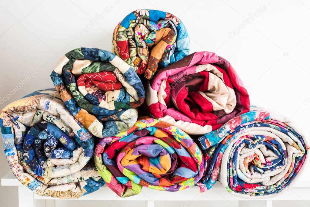 patchwork, sewing and fashion concept - bright beautiful quilts stacked in several rows in height for the storage, sale of finished stitched coverlets on white background, front view.