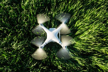 RUSSIA, ROSTOV-ON-DON - APRIL 20, 2017: superb modern white high-tech drone flying at low altitude on background of green field of grass, top view. clipart
