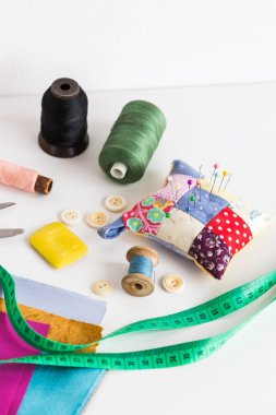 Araçlar closeup, patchwork, terzilik ve moda kavramı dikiş - ölçme bant, iş parçacığı makaralar, iğnelik, düğmeler, makas, renkli patchwork kumaş parçaları, beyaz masanın üzerinde dikey sabun.