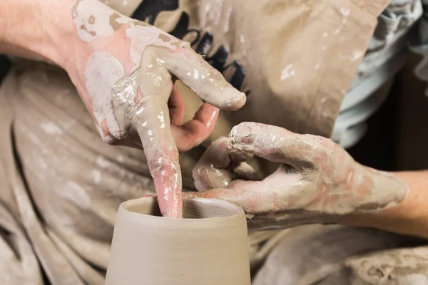 Workshop, aardewerk, keramiek kunst concept - bovenaanzicht op mans handen werk met potter wiel en ruwe klei, mannelijke vingers met water beeldhouwen sommige nieuwe kruik, close-up. — Stockfoto