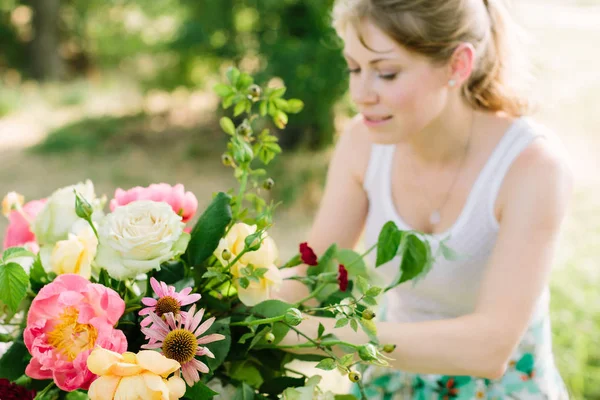 Casamento, desighn floral, verão, beleza, conceito de natureza - bela mulher de cabelos justos com rabo de cavalo fazendo buquê multicolorido brilhante com rosas, peônias rosa e cravo vermelho — Fotografia de Stock