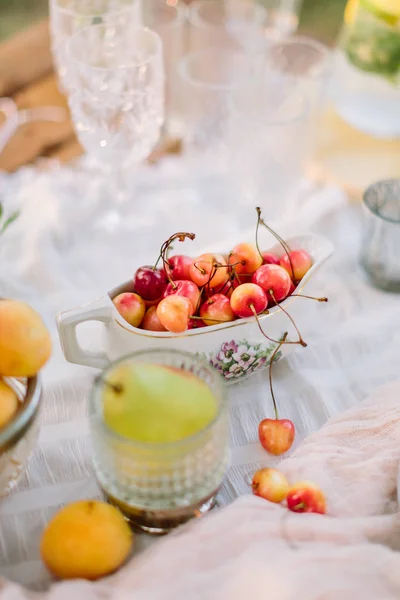 결혼식, 영양, 장식, 음식, 자연 개념-노란색과 빨간색 체리 크리스탈 와인 유리와 apricotes 근처 꽃 프린트와 그레이 비 보트에 누워 — 스톡 사진