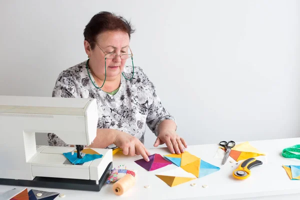 Κεντήματα και quilting στο εργαστήριο μιας γυναίκας ράφτης - ηλικιωμένες γυναίκες ράφτης θέσει στο desktop κομμάτια από χρωματιστό ύφασμα, γεννούν δίπλα στο ψαλίδι, κουμπιά, καρφίτσες και νήμα για ραπτομηχανή. — Φωτογραφία Αρχείου