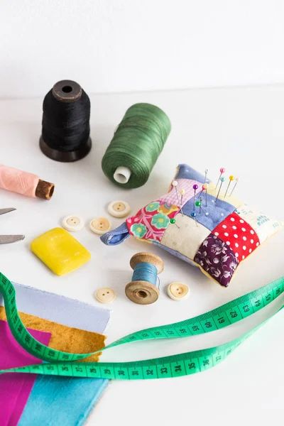 Araçlar closeup, patchwork, terzilik ve moda kavramı dikiş - ölçme bant, iş parçacığı makaralar, iğnelik, düğmeler, makas, renkli patchwork kumaş parçaları, beyaz masanın üzerinde dikey sabun.