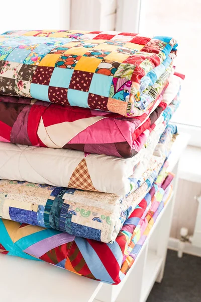 patchwork ve moda kavramı - güzel renkli yorgan, yatak örtüleri Muhafazası, beyaz zemin üzerine dikişli ürünlerin satışı için yükseklik içinde birkaç satır içinde yığılmış yığını.