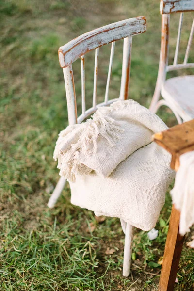 Picnic, muebles, concepto de decoración - sillas antiguas de madera vintage con alfombras que se encuentran en el picnic de verano cerca de una mesa de madera sobre hierba verde natural . — Foto de Stock