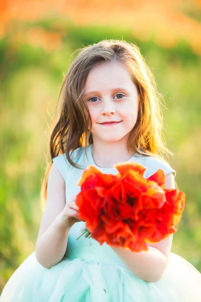 wedding, childhood, flora concept - portrait of beautiful girl of preschool age with sly smile and flowing light brown hair, shes wearing alice blue dress and holding bright bouquet of poppies