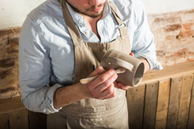 Potter, atölye, Seramik Sanat kavramı - kil Kupası ve araçları, bir esmer Fransız işyerinde, usta bir önlük giymiş ham ürün ile holding genç erkekler eller üzerinde yakın çekim.