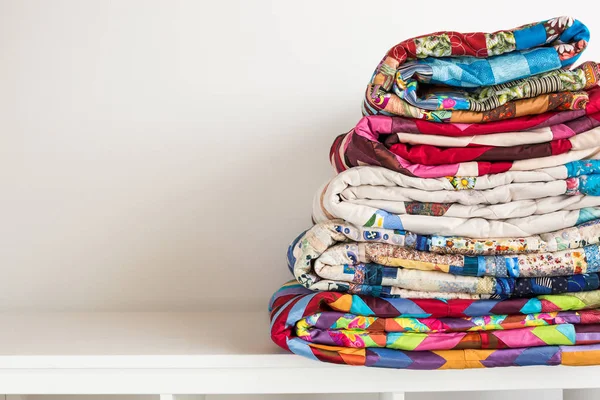 Concetto di cucito e moda - pila di trapunte colorate, bellissimi copriletti impilati in diverse file in altezza per lo stoccaggio, vendita di produzioni patchwork su sfondo bianco, spazio di copia . — Foto Stock