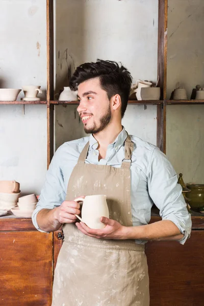 Potter, araçlar, Seramik Sanat kavramı - sakallı şamot, bir Fransız Atölyesi'nde pişmiş kap ile bitmiş sürahi holding genç usta eller bir önlük giymiş esmer erkek gülümseyen.