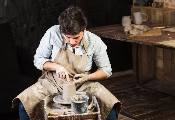 Cerâmica, oficina, conceito de arte cerâmica - jovem mestre masculino trabalha com mãos e roda de oleiro, morena dedos masculinos esculpir algum jarro novo de argila crua com água, close-up . — Fotografia de Stock