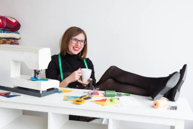 dikiş ve kapitone bir terzi - çay güzel bir gülümseyerek terzi kadının bir masada bir dikiş makinesi, kumaş ve konu ile bir iş ara atölye